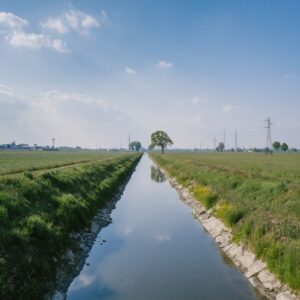 A serene rural water canal with grassy banks under a bright blue sky.